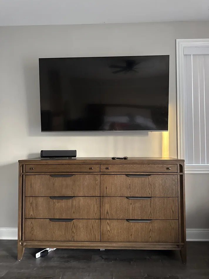 Large TV mounted flat on a bedroom wall above a wooden dresser