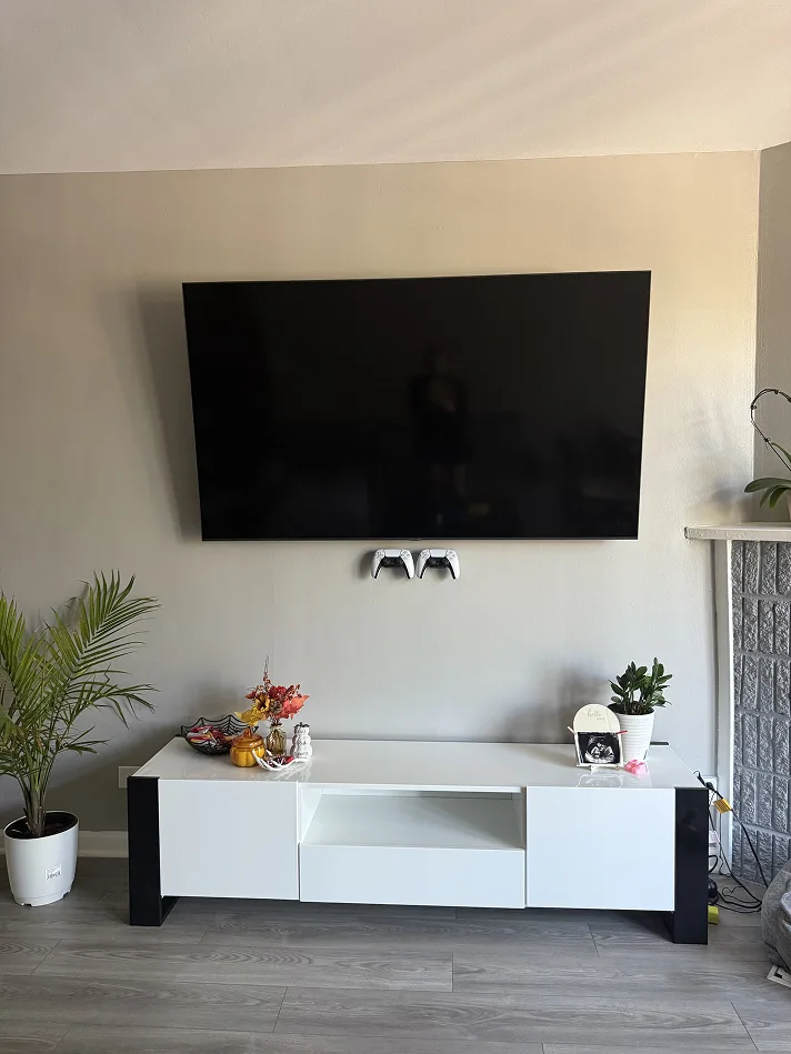 Wall-mounted TV with no cables below it, above a low white media unit