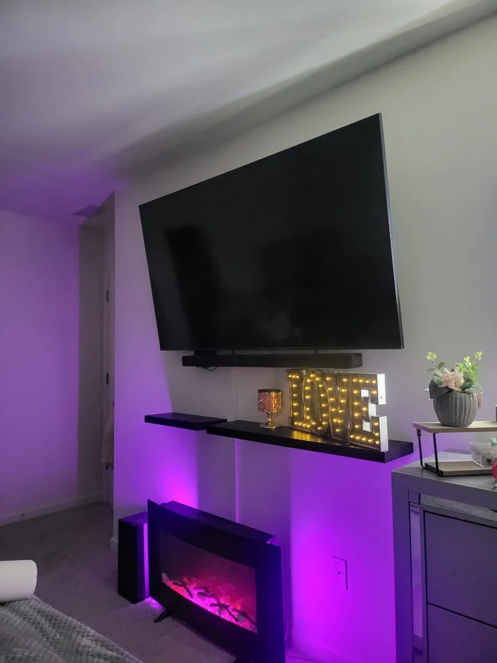 TV angled on a full-motion mount above floating shelves and an electric fireplace