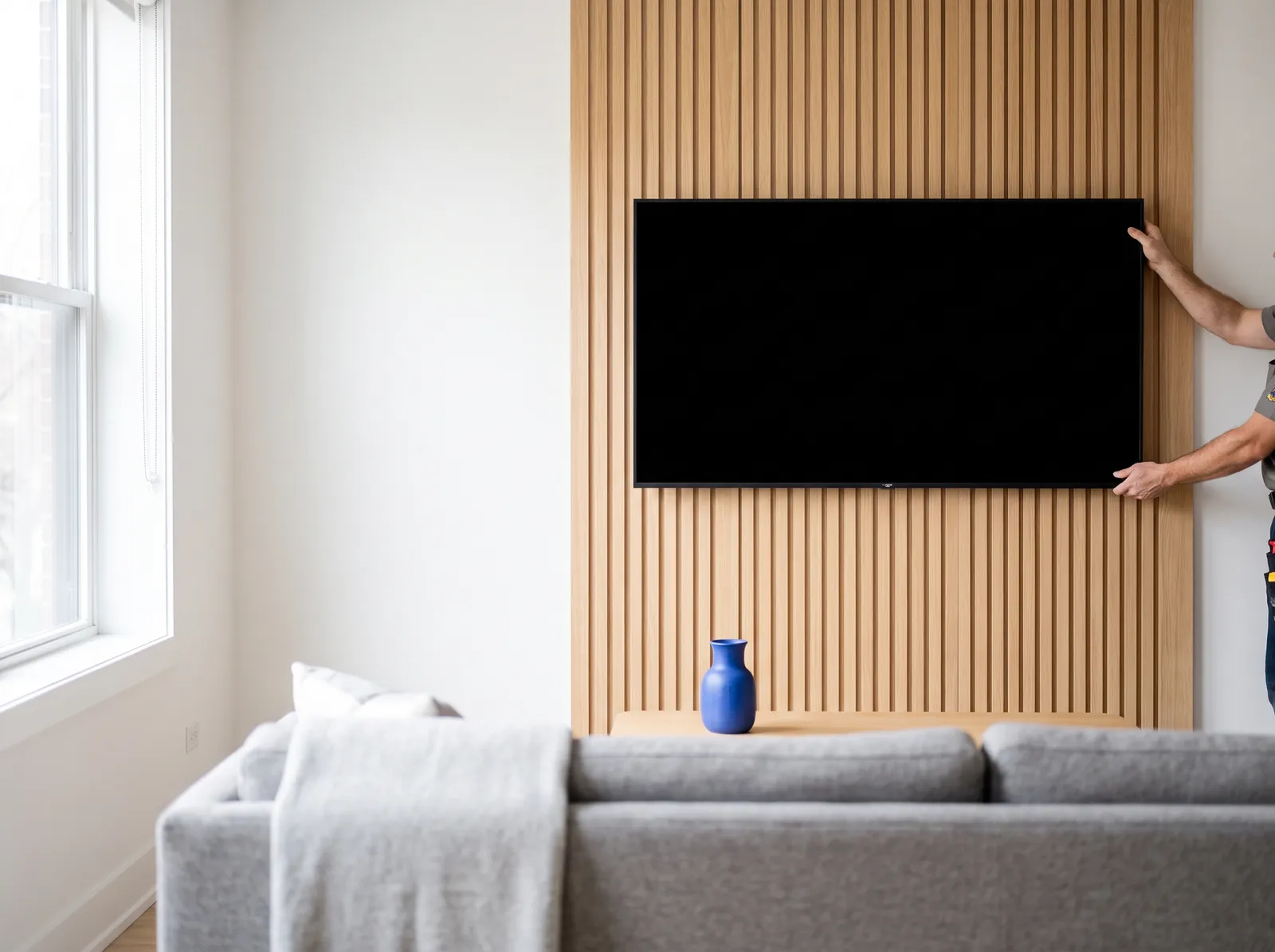 Installer centering a TV on a light oak slat wall